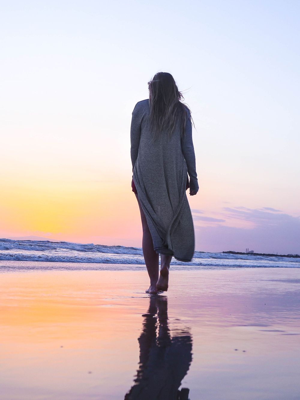 A woman walking alone along the shoreline in soft evening light